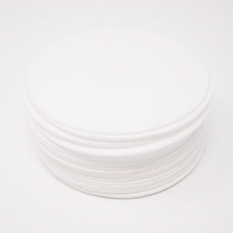 A neat stack of round white synthetic filter discs on a white surface