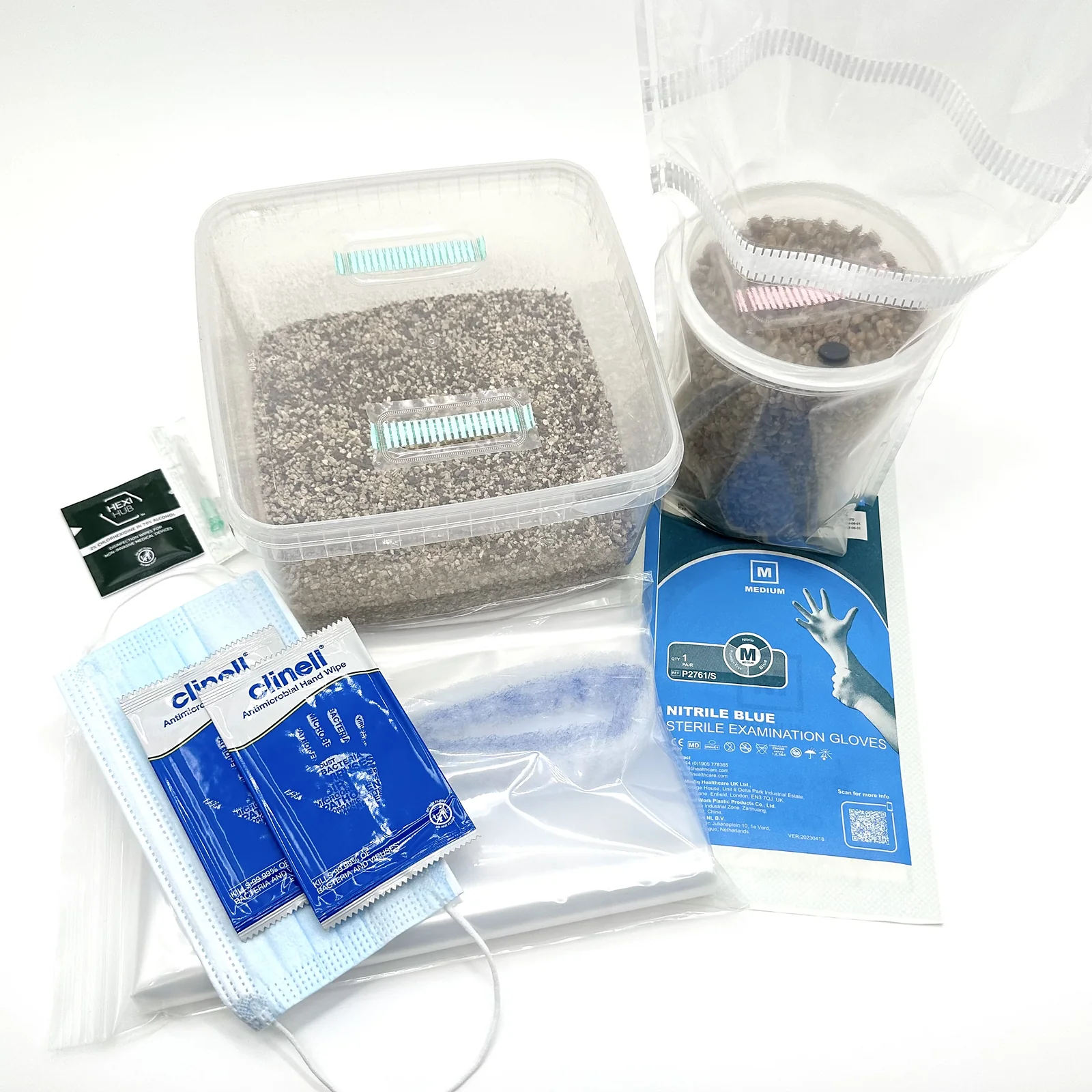 The MonoBox grow kit from above: the substrate tub beside a bagged grain jar, with medium nitrile gloves, a face mask, Clinell wipes, an alcohol wipe and a liner bag arranged around them
