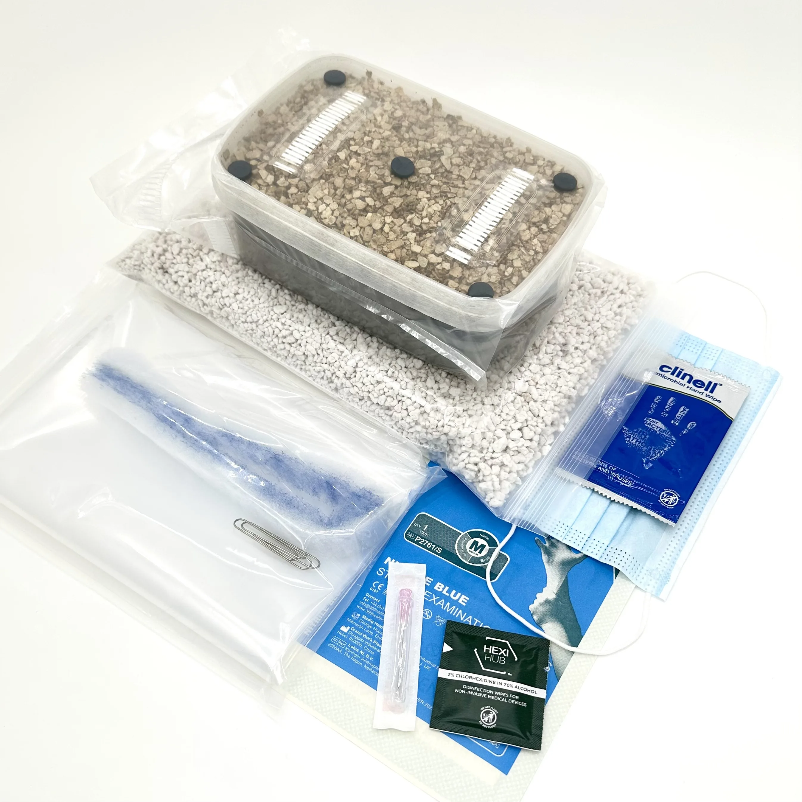 Everything included in the Grow Kit version of the XL Cylocybe Special MykoBox, laid out together: the sealed grow tub with its filter strips and injection ports, a bag of perlite, a liner bag, nitrile gloves, a face mask, alcohol and chlorhexidine wipes, and a sterile syringe