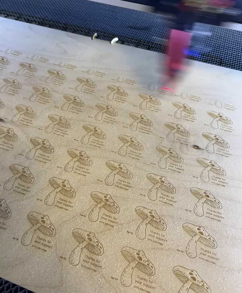Thank-you cards being laser engraved on wood: mushrooms with Thanks for your support and the Cylocybe logo